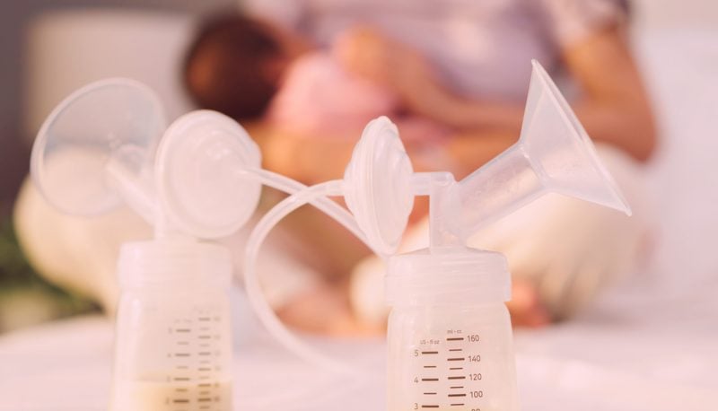 Two breast pumps in foreground, nursing mother sitting out of focus in background