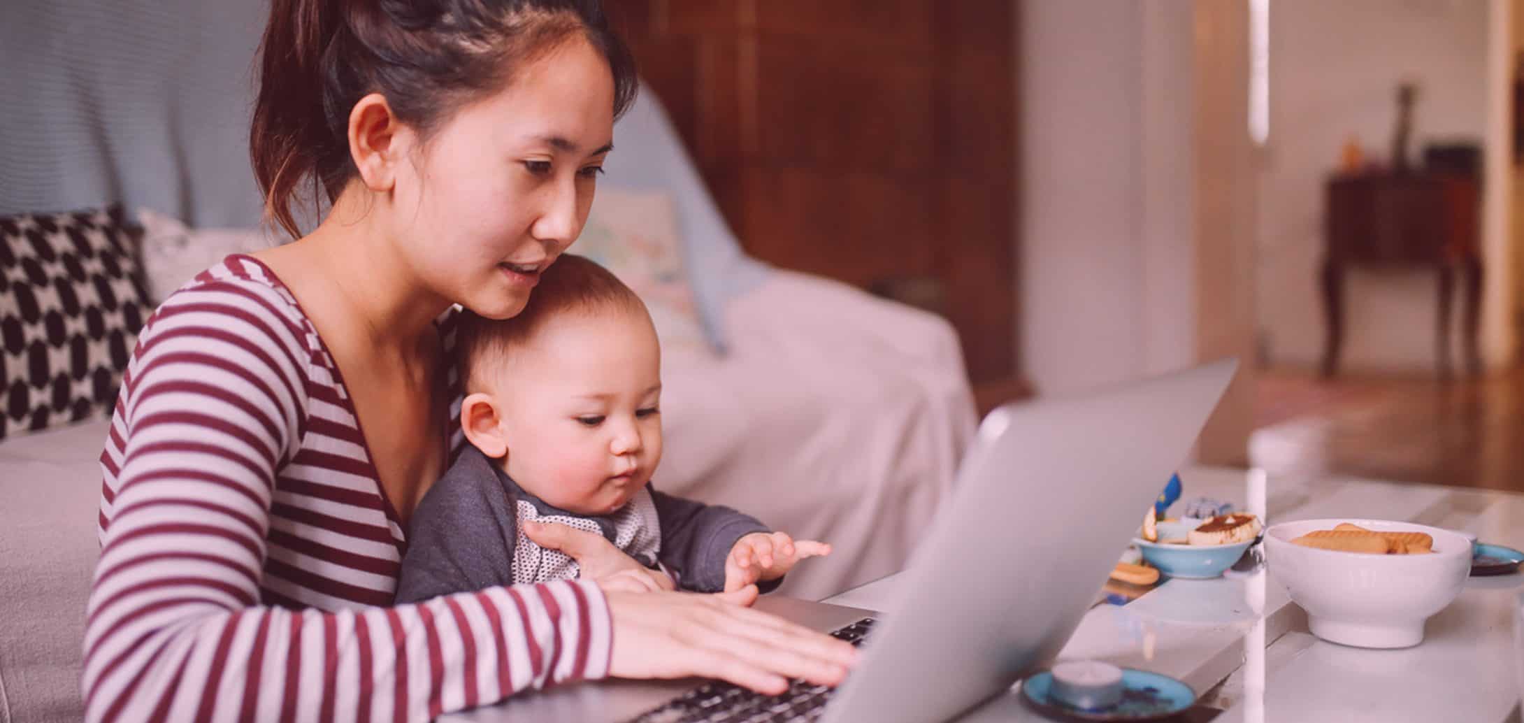 Mother with her infant child in her lap while working from home on her laptop