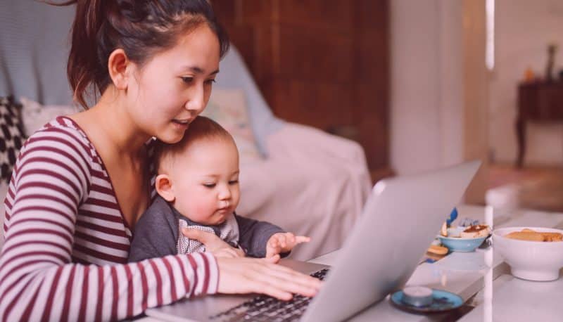 Mother with her infant child in her lap while working from home on her laptop