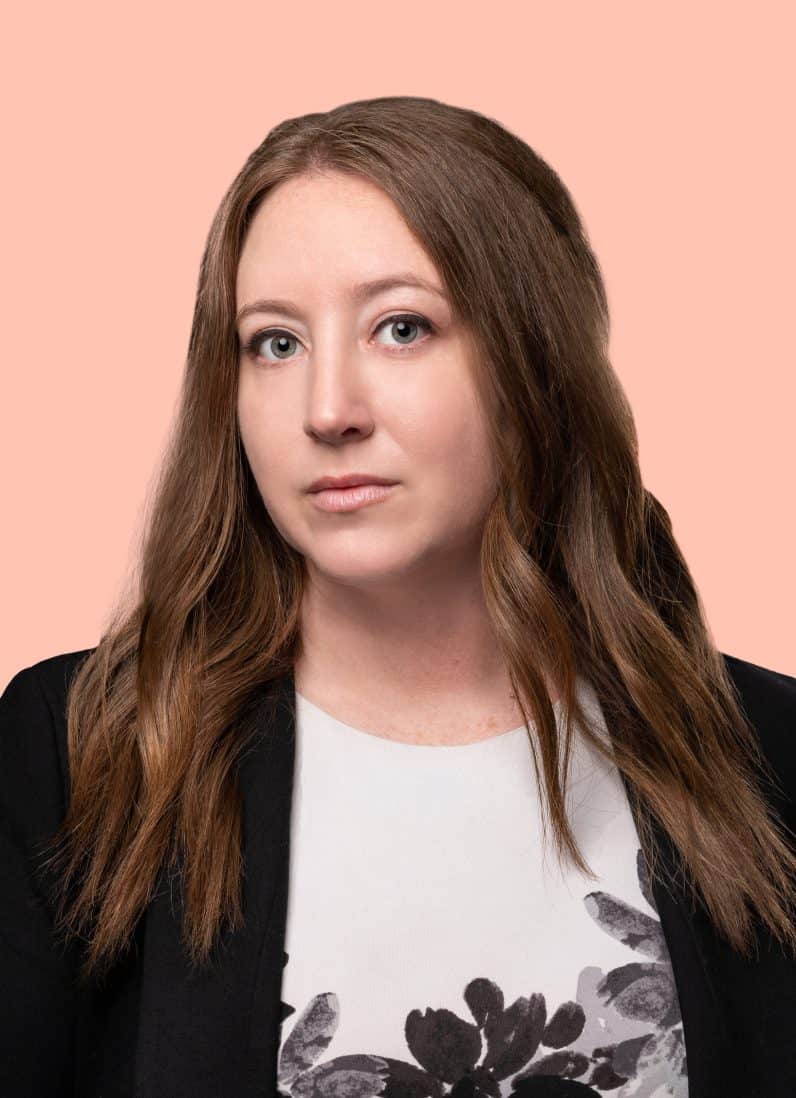 Aliza Grossman attorney wearing a black blazer and white top with black flowers on a peach background