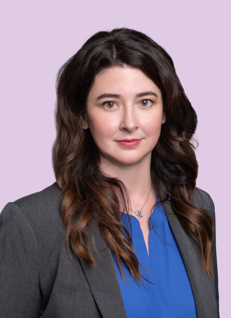 Brittany Shaw attorney wearing a gray blazer, blue shirt and long hair on lavendar background