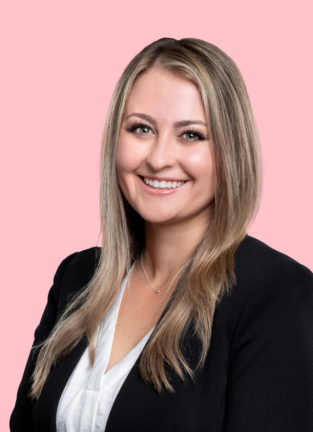 Melissa Rinehart attorney long blonde hair wearing black blazer, white blouse on a pink background smiling at camera