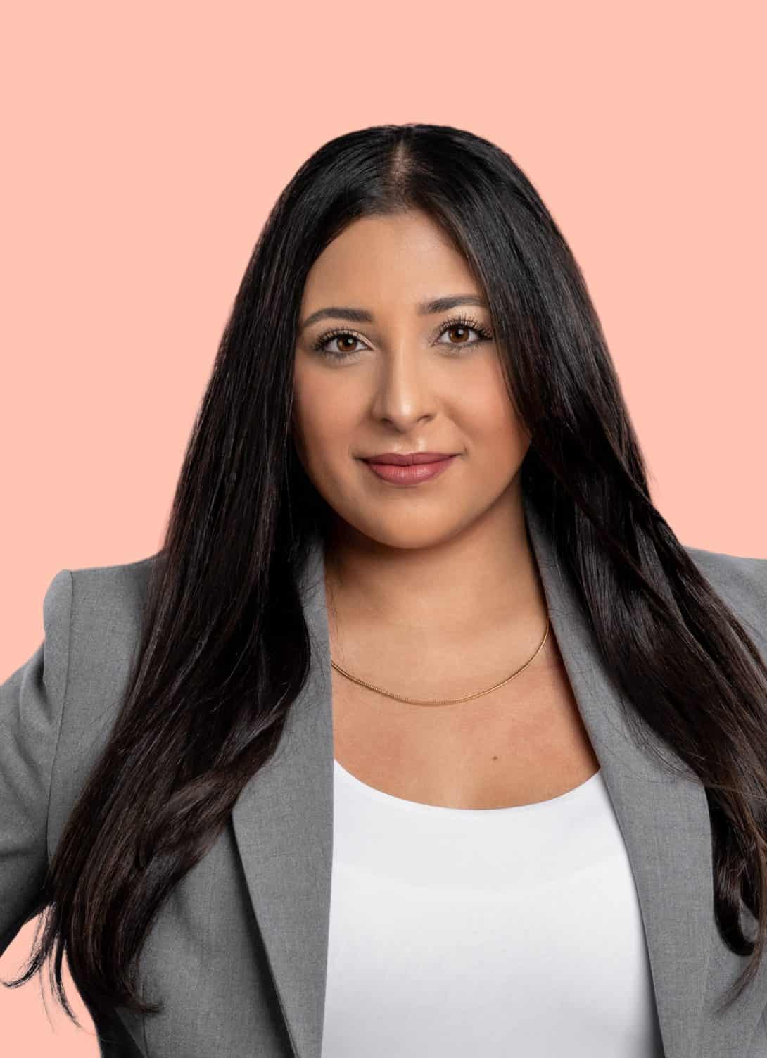 Yasmin Hosseini portrait looking at camera, chest up, wearing gray blazer, white top with long straight brunette hair