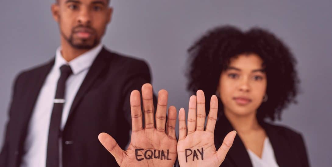 One male and one female worker in suits holding their open hands to the camera with "EQUAL PAY"  written on their palms.