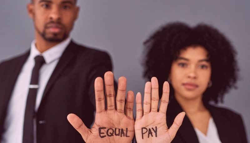 One male and one female worker in suits holding their open hands to the camera with "EQUAL PAY" written on their palms.